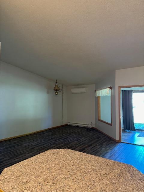 spare room featuring baseboard heating, dark hardwood / wood-style floors, a wall mounted air conditioner, a textured ceiling, and vaulted ceiling