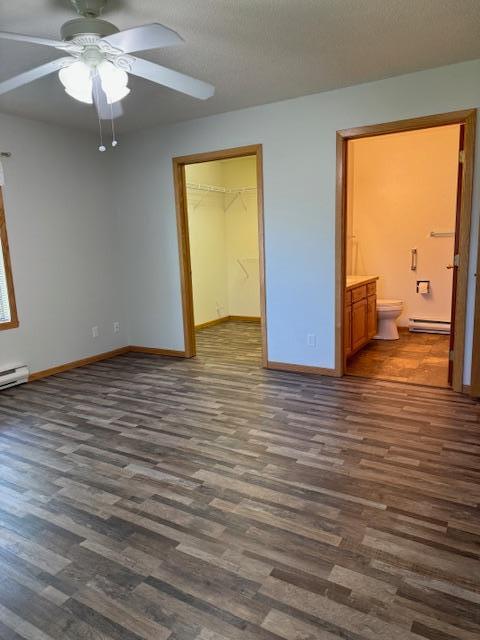 unfurnished bedroom featuring a baseboard radiator, dark hardwood / wood-style flooring, a textured ceiling, and a spacious closet