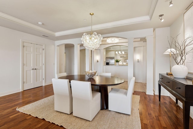 dining room featuring hardwood / wood-style floors, decorative columns, a tray ceiling, crown molding, and an inviting chandelier