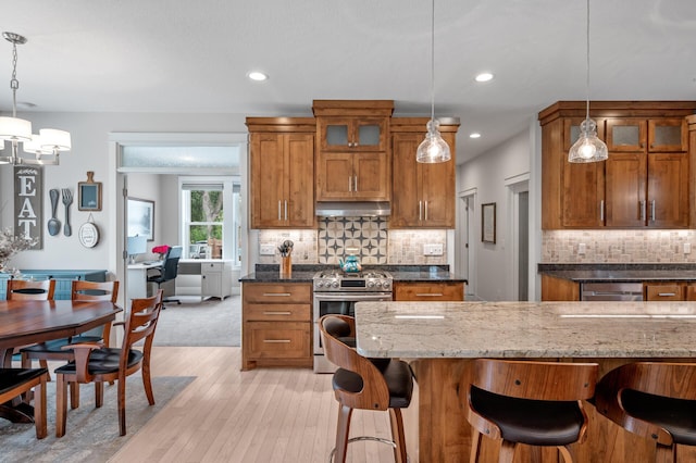 kitchen featuring dark stone counters, light hardwood / wood-style flooring, stainless steel appliances, backsplash, and decorative light fixtures