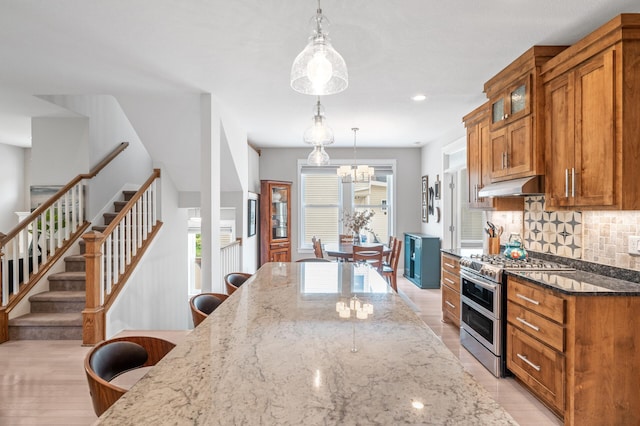 kitchen featuring backsplash, light hardwood / wood-style flooring, decorative light fixtures, double oven range, and dark stone counters