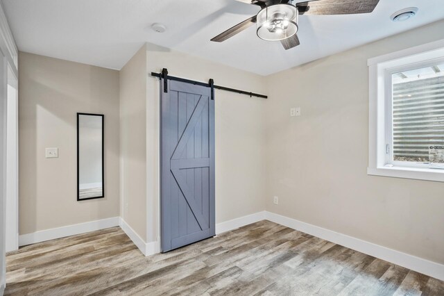 unfurnished room featuring ceiling fan, light hardwood / wood-style floors, a barn door, and a healthy amount of sunlight