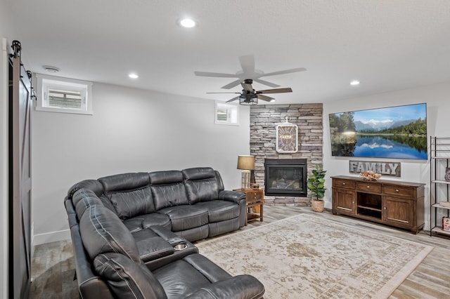 living room with ceiling fan, a stone fireplace, and light hardwood / wood-style floors