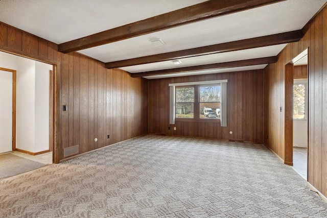 spare room with beamed ceiling, light colored carpet, and wooden walls