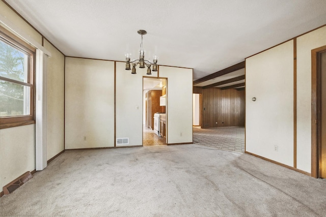 carpeted empty room featuring beam ceiling and a chandelier