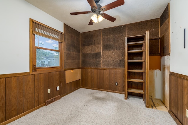 spare room with ceiling fan, light colored carpet, and wooden walls