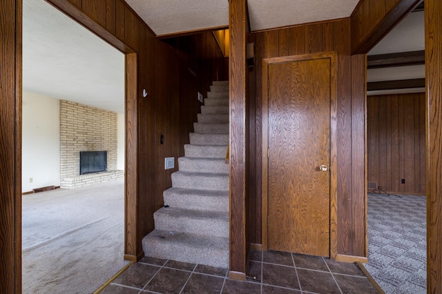 stairs with wooden walls, carpet, a textured ceiling, and a brick fireplace