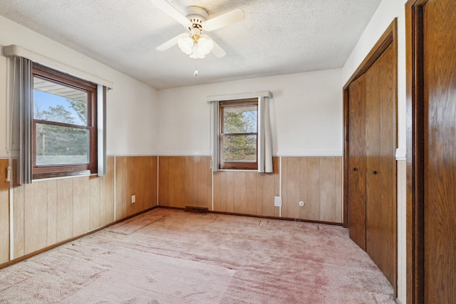 carpeted spare room featuring a textured ceiling, ceiling fan, and wooden walls