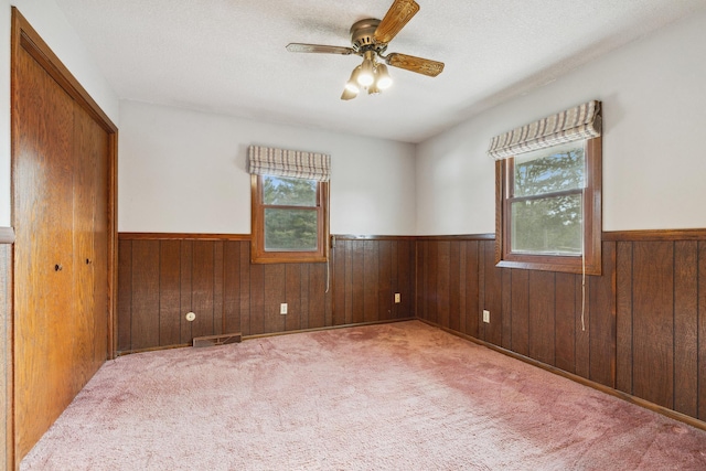 empty room featuring carpet flooring, ceiling fan, a textured ceiling, and wood walls