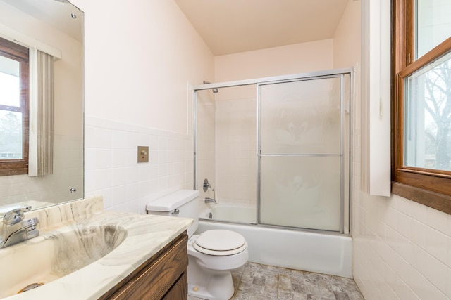 full bathroom featuring vanity, toilet, tile walls, and combined bath / shower with glass door