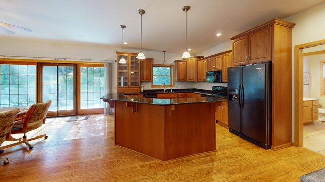 kitchen featuring brown cabinets, a breakfast bar area, glass insert cabinets, a kitchen island, and black appliances