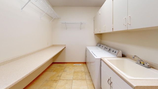 clothes washing area with a sink, baseboards, cabinet space, washing machine and clothes dryer, and stone tile flooring