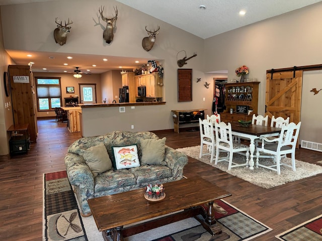 living area with visible vents, dark wood-type flooring, a barn door, high vaulted ceiling, and a ceiling fan