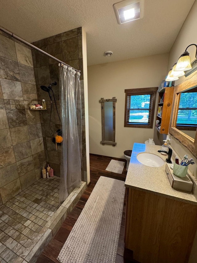 bathroom with visible vents, a textured ceiling, wood finished floors, a shower stall, and vanity