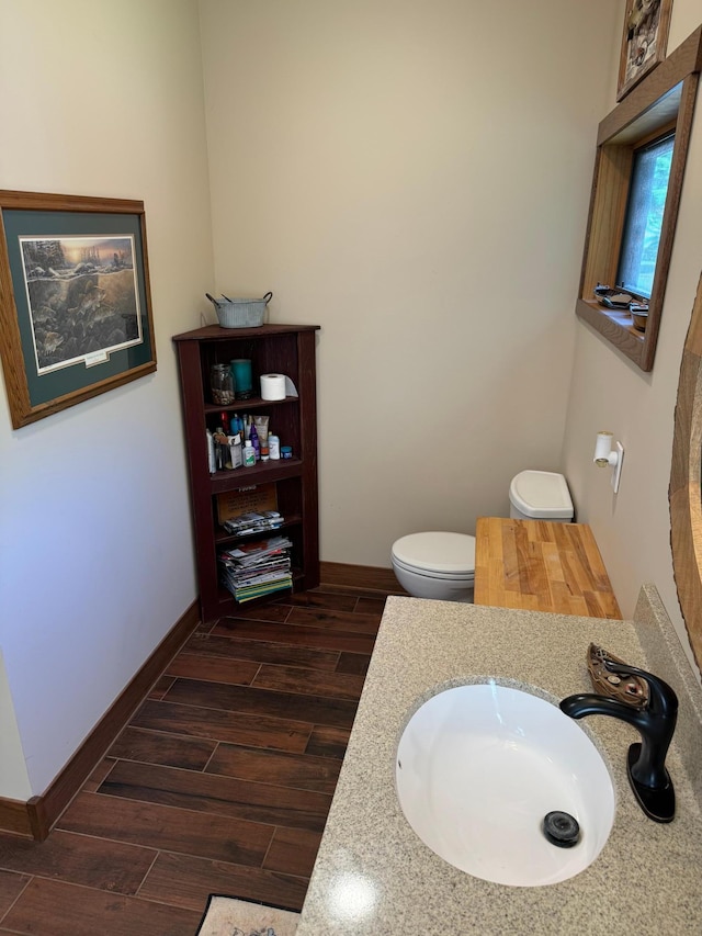 bathroom featuring a sink, baseboards, wood finish floors, and toilet