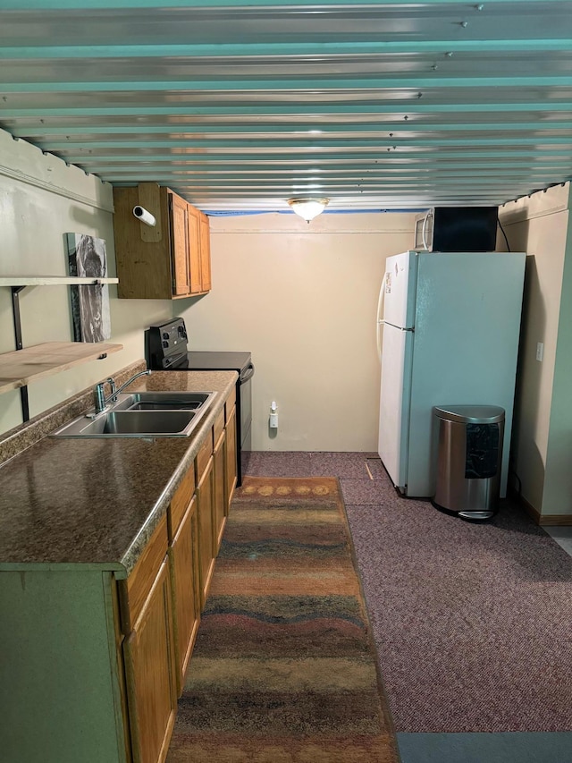 kitchen featuring freestanding refrigerator, a sink, black range with electric stovetop, dark countertops, and brown cabinets