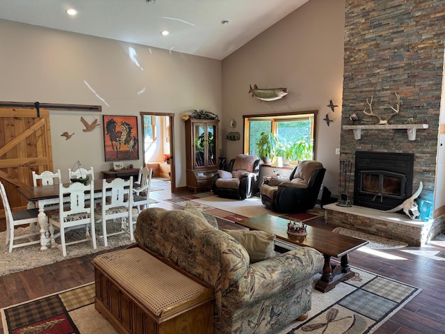 living area with a barn door, a stone fireplace, recessed lighting, wood finished floors, and high vaulted ceiling