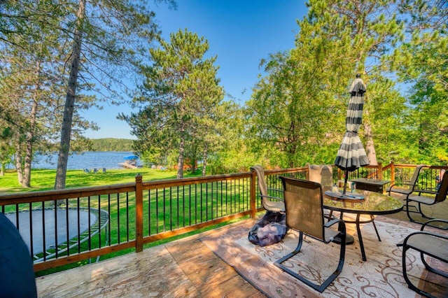 deck featuring outdoor dining area, a yard, and a water view