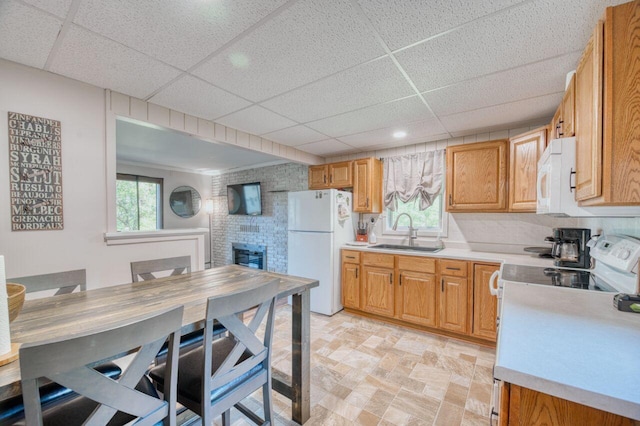 kitchen featuring a healthy amount of sunlight, a brick fireplace, light countertops, white appliances, and a sink