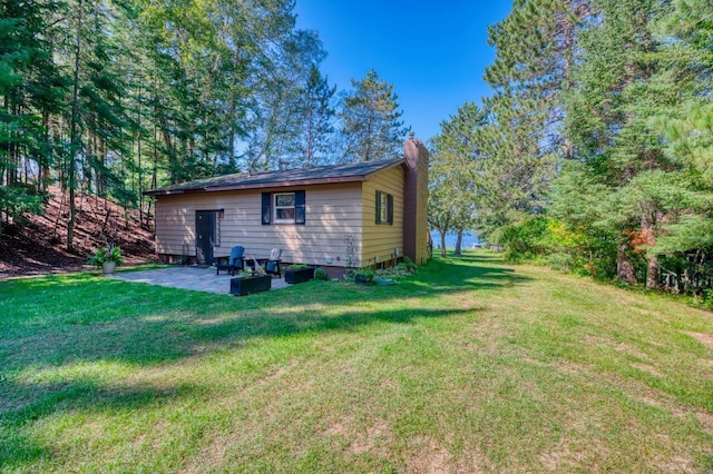 rear view of property featuring a patio area, a lawn, and a chimney