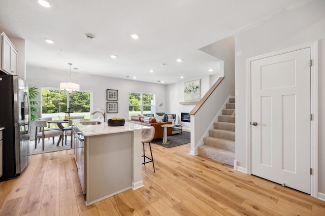 kitchen with a kitchen breakfast bar, light hardwood / wood-style floors, an island with sink, stainless steel appliances, and decorative light fixtures