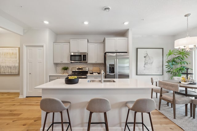 kitchen featuring pendant lighting, sink, a center island with sink, light hardwood / wood-style flooring, and stainless steel appliances