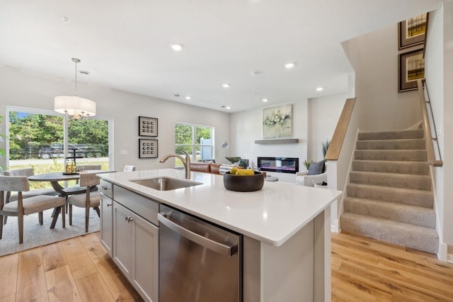 kitchen with an island with sink, light wood-type flooring, dishwasher, and decorative light fixtures