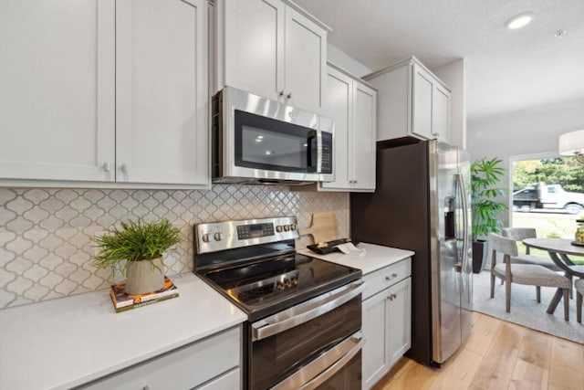 kitchen with light wood-type flooring, white cabinets, appliances with stainless steel finishes, and backsplash