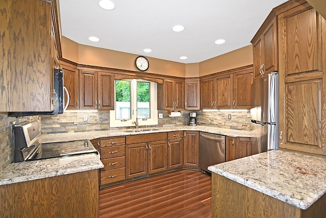 kitchen featuring light stone countertops, dark wood-style flooring, a sink, appliances with stainless steel finishes, and decorative backsplash