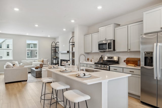 kitchen with sink, a kitchen breakfast bar, a center island with sink, appliances with stainless steel finishes, and light wood-type flooring