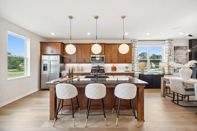 kitchen with light wood-type flooring, appliances with stainless steel finishes, a wealth of natural light, and a kitchen island with sink