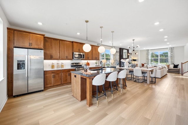 kitchen featuring pendant lighting, appliances with stainless steel finishes, a breakfast bar area, a center island with sink, and light hardwood / wood-style floors