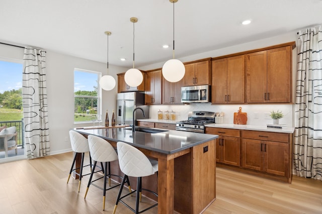 kitchen with backsplash, appliances with stainless steel finishes, light hardwood / wood-style floors, sink, and a kitchen island with sink