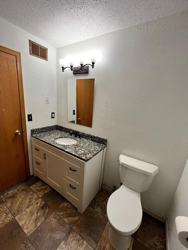 bathroom with a textured ceiling, vanity, and toilet