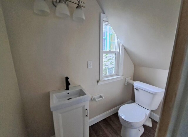 bathroom with wood-type flooring, vanity, toilet, and vaulted ceiling