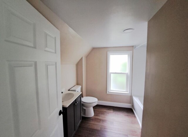 bathroom with vanity, toilet, a tub, hardwood / wood-style flooring, and vaulted ceiling