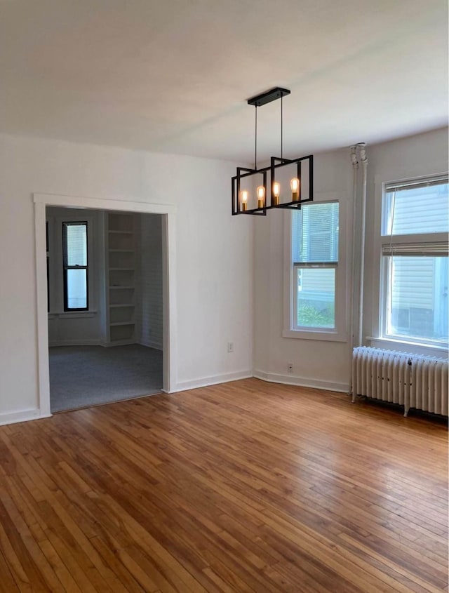 empty room featuring radiator heating unit, light hardwood / wood-style flooring, and an inviting chandelier