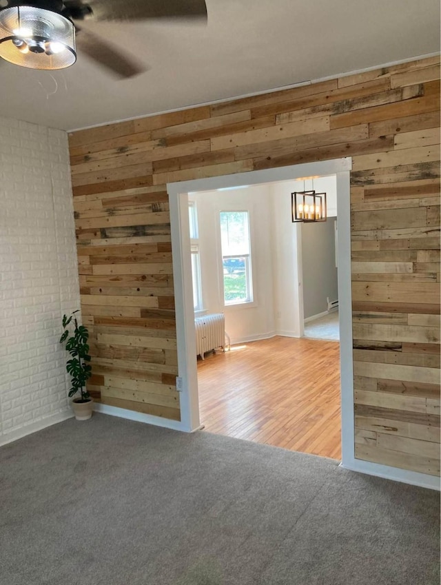 unfurnished room with ceiling fan, radiator, hardwood / wood-style flooring, and wooden walls