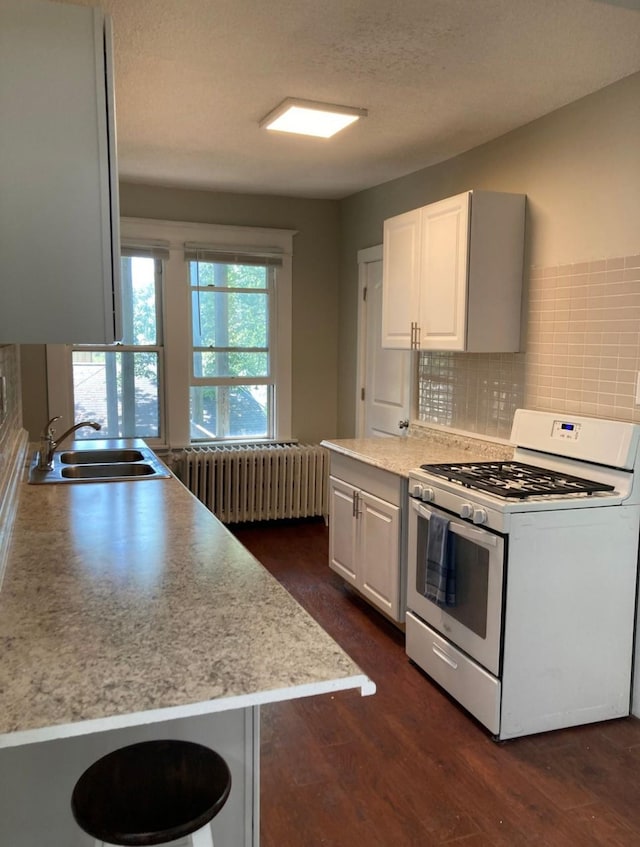 kitchen featuring radiator, tasteful backsplash, white cabinetry, white range with gas stovetop, and dark hardwood / wood-style flooring