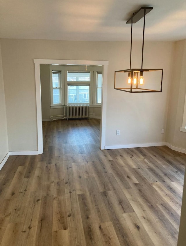 unfurnished dining area featuring radiator, hardwood / wood-style flooring, and a notable chandelier