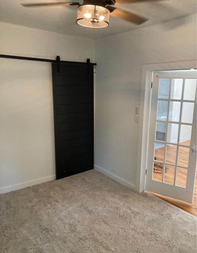 unfurnished room featuring a barn door, hardwood / wood-style floors, and ceiling fan