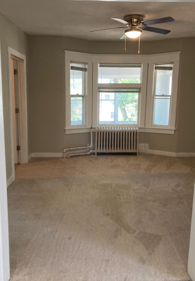 carpeted empty room with ceiling fan, radiator heating unit, and plenty of natural light