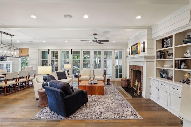 living room featuring dark wood finished floors, a brick fireplace, recessed lighting, and ceiling fan with notable chandelier