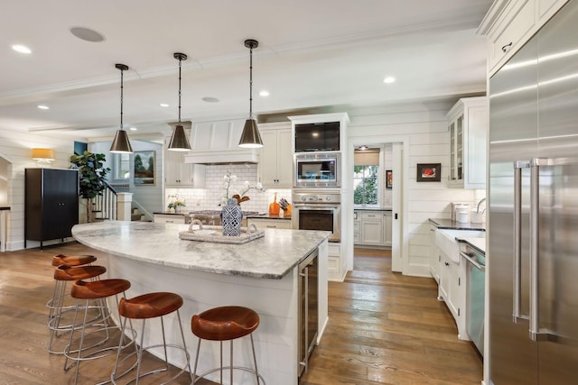 kitchen featuring dark hardwood / wood-style flooring, hanging light fixtures, built in appliances, a center island, and white cabinetry