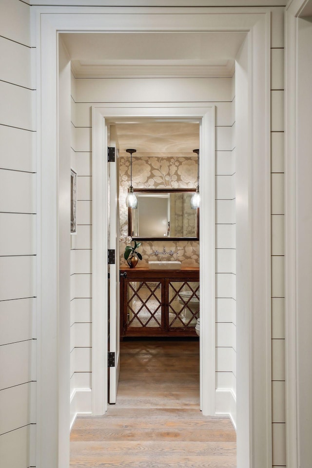 corridor with wallpapered walls, crown molding, and wood finished floors