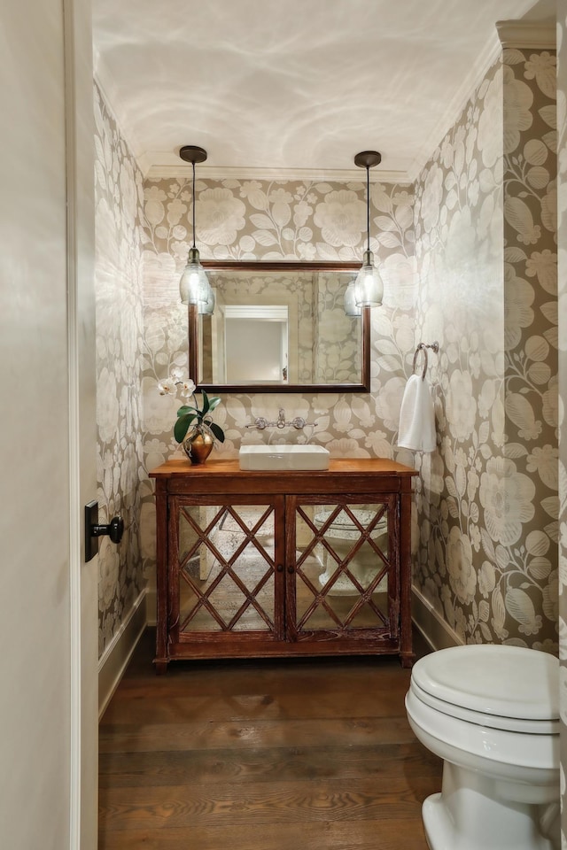 bathroom featuring toilet, wood finished floors, crown molding, wallpapered walls, and vanity