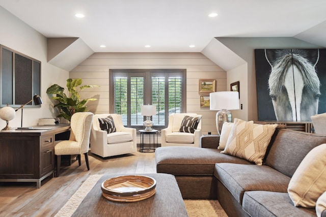 living room with vaulted ceiling, wood walls, and light hardwood / wood-style floors