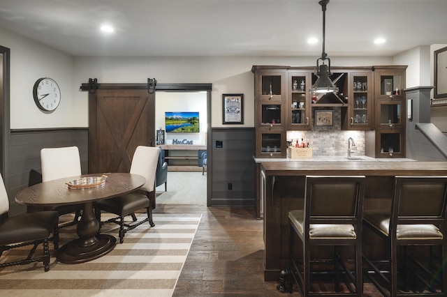 bar featuring dark brown cabinetry, hanging light fixtures, dark hardwood / wood-style floors, a barn door, and decorative backsplash