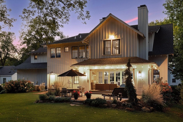 back house at dusk featuring outdoor lounge area, a patio, and a yard