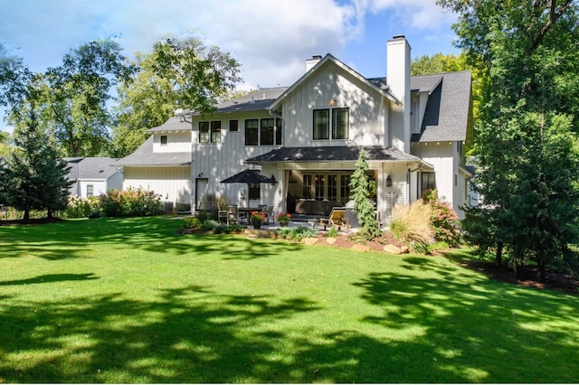 rear view of property featuring a lawn, board and batten siding, a chimney, and a patio area